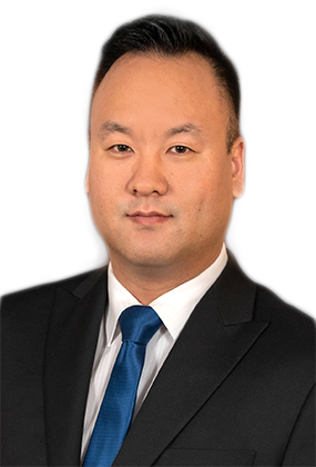 A photograph of Daniel Kim, AS3 Office Manager, is shown on a dark-grey background. Daniel is an Asian male wearing a black suit coat, white dress shirt, and a navy blue tie. He has short black hair and a slightly darker complexion, and is smiling | AS3 Med Spa