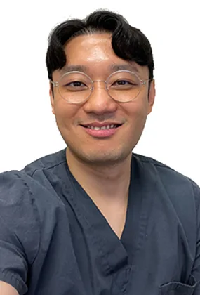 An image of Tony Kim, RN, an AS3 Nurse Injector, is shown. The image displays an Asian man wearing a dark blue scrub top. The model has short black wavy hair | AS3 Med Spa